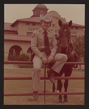 Jim Lane sitting on fence next to horse in front of the Live Stock Exchange Building.