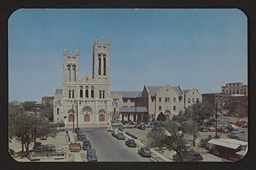 The image shows a slightly elevated view of a downtown Fort Worth street leading to the front exterior of the church. There are cars parked on either side of the street.