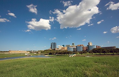 Fort Worth skyline with grassy meadow in foreground, partly cloudy sky above