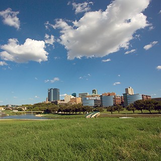 Fort Worth skyline, grassy field, partyly cloudy sky