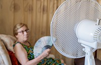 elderly woman holding fan, electric fan in foreground